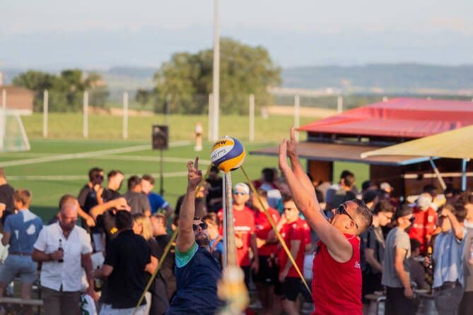 Beachvolleyball-Sprung am Netz, dahinter Party-Stimmung an der Bier-Bar.